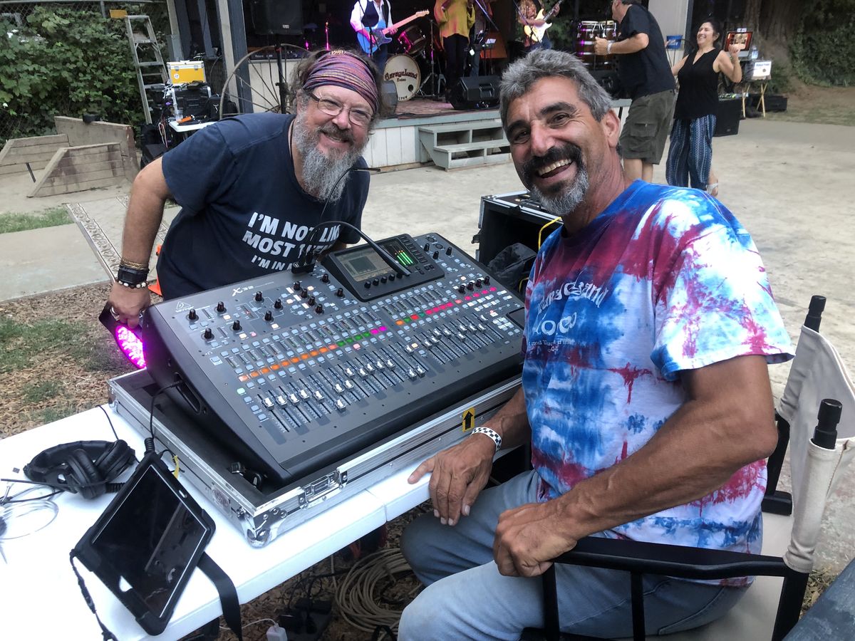 Two Sound Travels crew members smiling at the X32 console during an outdoor show